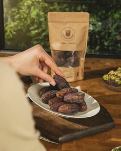 a person picking dates from a plate on a wooden table next to a bag of dried fruit