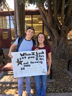 two people standing next to each other holding a sign that says what i look at you