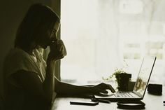 a woman sitting in front of a laptop computer on top of a wooden table next to a plant