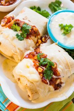 three burritos on a plate with salsa and sour cream dip in the background