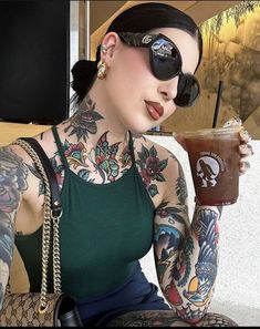 a woman with tattoos holding a drink in her right hand and wearing sunglasses on top of her head