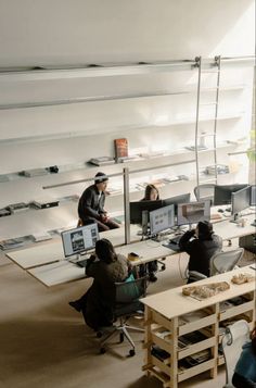 people sitting at desks working on computers in an open room with lots of shelves