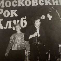 two men standing next to each other in front of a sign with words on it