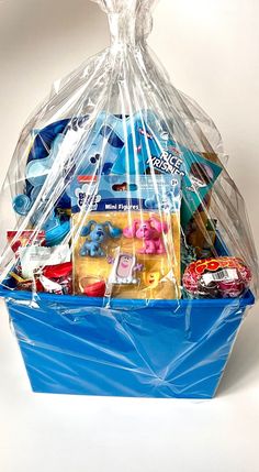 a blue plastic basket filled with toys and candy items on a white background in the shape of a shopping bag