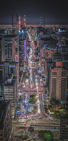 an aerial view of a city at night with cars driving on the street and tall buildings in the background