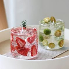 two glasses filled with water and strawberries on top of a table next to each other