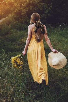 a woman in a yellow dress is walking through the grass with a straw hat on her head