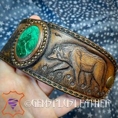 "\"Silver Shadow\" is a hand tooled leather cuff bracelet with carved fir forest, wolf and malachite lake. For those who's hearts are close to nature, Paganism, Wiccan, fantasy style. The cuff was made for a 7 1/2\" wrist. This exclusive piece wasn't made with special stamps or craftaids, just basic craft tools and my creativity. It's my design, I use my hands & imagination and add a piece of my soul into any item I make, so each of them is made with love. This particular bracelet was MADE TO OR Green Leather Artisan Jewelry, Green Leather Jewelry Gift, Green Leather Jewelry As A Gift, Green Leather Jewelry For Gifts, Unique Engraved Cuff Bracelet As Gift, Unique Engraved Cuff Bracelet For Gift, Luxury Leather Bangle Jewelry, Luxury Adjustable Engraved Leather Bracelet, Handmade Custom Leather Bracelet