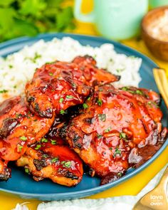 a blue plate topped with meat covered in sauce next to rice and chopsticks