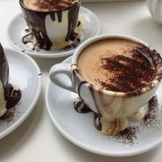 three cups filled with different types of desserts on top of white plates and saucers