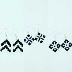 three black and white pixelated earrings are hanging from silver ear wires on a white surface