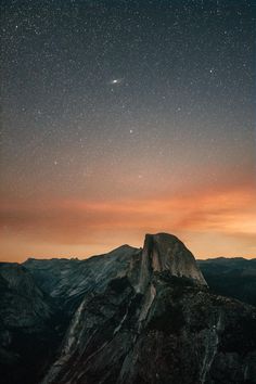 the night sky is filled with stars above a mountain top and mountains in the distance