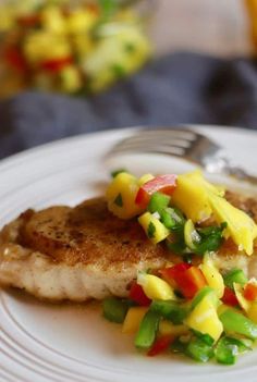 a white plate topped with fish covered in mango salsa