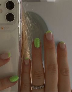 a woman's hand with green and white nail polish on it next to a cell phone