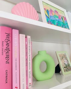 some books are on a white shelf with pink and green items in front of them