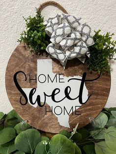 a wooden sign that says home sweet home with flowers on top and greenery around it