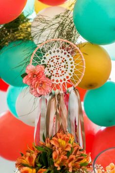 an arrangement of flowers and balloons in front of a wall hanging with a dream catcher on it