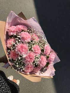 a bouquet of pink carnations and baby's breath is held by someone