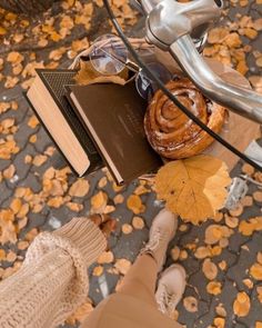 a person standing next to a bike with a book and some leaves on the ground