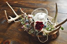 an antler head with flowers and candles in it on a wooden table next to a candle holder