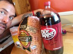 a man sitting at a table next to a bottle of dr pepper and a bag of chips