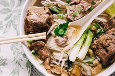 a bowl filled with meat, noodles and veggies next to chopsticks