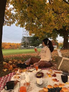 a woman sitting on top of a picnic table covered in food and drinks next to trees