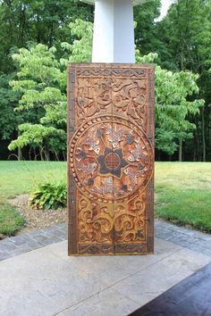 an intricately carved wooden door in the middle of a yard with grass and trees behind it