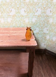 an orange vase sitting on top of a wooden table next to a wallpapered wall