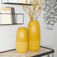 two yellow vases sitting on top of a table next to each other with flowers in them