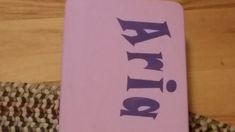 a pink book with purple letters on it sitting on top of a woven table cloth