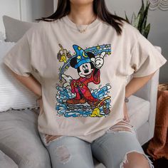 a woman sitting on top of a couch wearing a mickey mouse shirt and ripped jeans