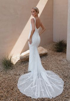 a woman in a white wedding dress standing on gravel ground with her back to the camera