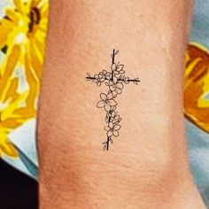 a small cross tattoo on the ankle with flowers around it and an arrow in the middle