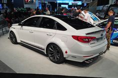 a white car is on display at an auto show while people look around the vehicle