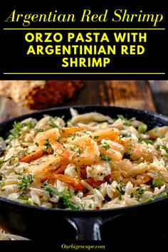 a skillet filled with pasta and shrimp on top of a wooden table next to bread