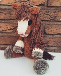 a brown and white stuffed horse sitting next to a brick wall with snow on the ground