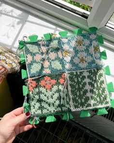 a person holding four pieces of knitted fabric in front of a window sill