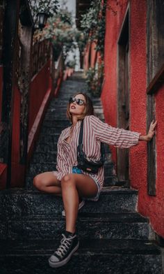 a woman is sitting on the steps in front of red buildings with her arms outstretched