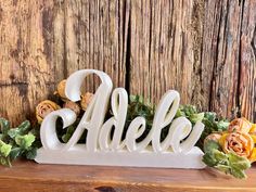 a white wooden name sign sitting on top of a table next to flowers and greenery