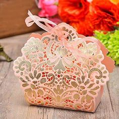 a pink box with an intricate design on the lid and ribbon tied around it, sitting next to flowers