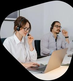 two people sitting at a table with laptops and headphones in front of them