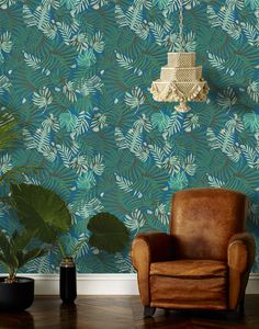 a brown chair sitting in front of a wall with green leaves on it and a chandelier hanging from the ceiling