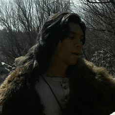 a man in a fur coat standing next to trees and rocks with his eyes closed