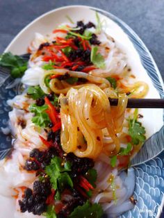 a plate filled with noodles and vegetables on top of a blue and white plate next to chopsticks