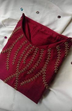 a red cloth with gold beading on it sitting on top of a white sheet