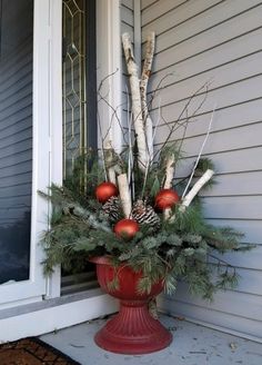 a red vase filled with pine cones and ornaments on the front door sill next to a window