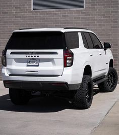 a white truck is parked in front of a brick building with black rims and tires