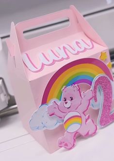 a pink box with a teddy bear holding a rainbow and the number two on it