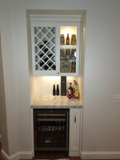 a small kitchen with white cabinets and marble counter tops, along with a wine rack